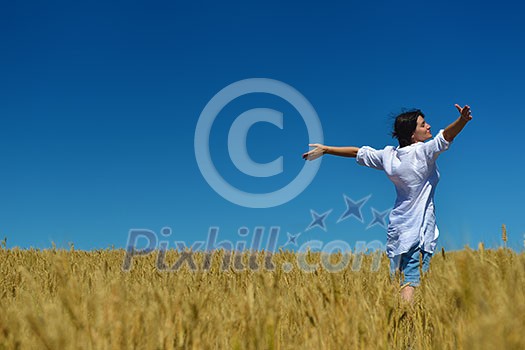 Young woman standing jumping and running  on a wheat field with blue sky in  background at summer day representing healthy life and agriculture concept