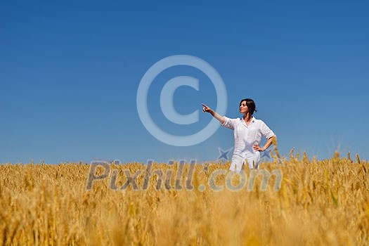 Young woman standing jumping and running  on a wheat field with blue sky the background at summer day representing healthy life and agriculture concept