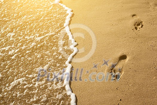 Traces of feet in the sand on the beach and a wave washed them