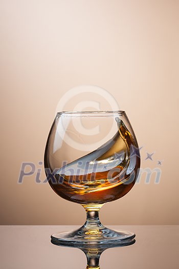 Splash of cognac in glass on brown background Splash of cognac in glass on brown background