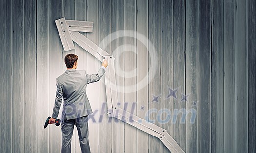 Rear view of businessman fixing wooden graph arrow with drill Rear view of businessman fixing wooden graph arrow with drill
