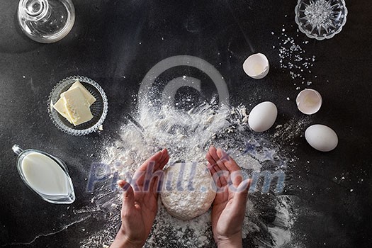 Woman's hands knead dough on table with flour and ingridients. Top view. Woman's hands knead dough on table with flour and ingridients. Top view.