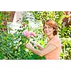 Happy woman gardening and pruning rose bush with garden shears