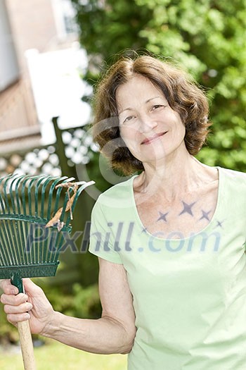 Senior woman smiling holding rake and gardening outside Senior woman smiling holding rake and gardening outside