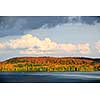 Forest of colorful autumn trees with lake and dramatic sky