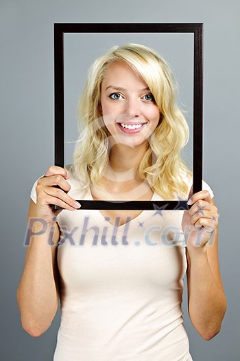Portrait of smiling young woman holding picture frame on grey background