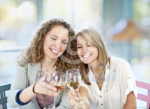 Two happy women in cafe celebrating with glasses of white wine