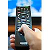 Hand holding television remote control pressing buttons