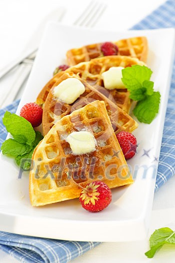 Plate of belgian waffles with fresh strawberries and pats of butter