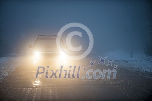 Bright headlights of a car driving on foggy winter road