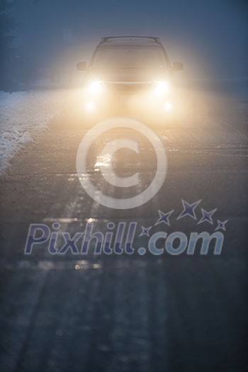 Bright headlights of a car driving on foggy winter road