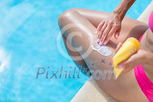 Attractive, young woman with healthy skin applying suncream by a pool (shallow DOF; color toned image)