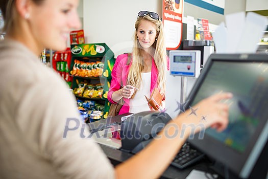 Beautiful young woman paying for her groceries at the counter of a grocery store/supermarket (color toned image)