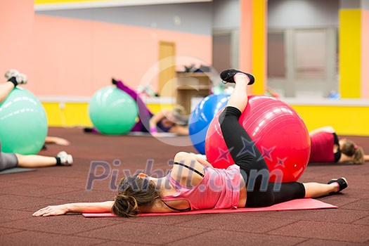 Group people in a pilates class at the gym - young woman with gymball at fitness training (shallow DOF, color toned image)