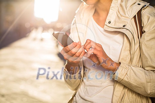 Young woman messaging/using app on her smart-phone in a city street context (shallow DOF; color toned image)