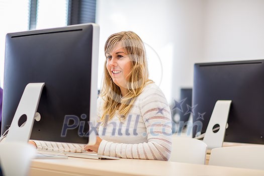 Female student/ businesswoman using a desktop computer staying up to date, working (color toned image; shallow DOF)