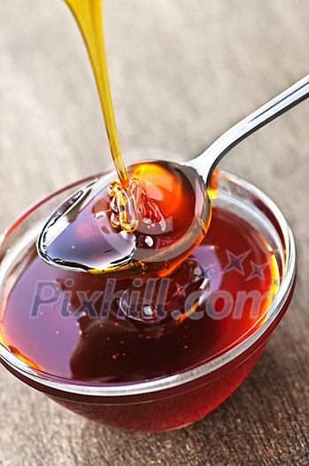 Thick golden honey drizzling onto spoon and bowl