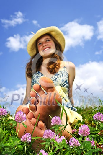 Young teenage girl sitting on summer meadow amid wildflowers in straw hat Young teenage girl sitting on summer meadow amid wildflowers in straw hat