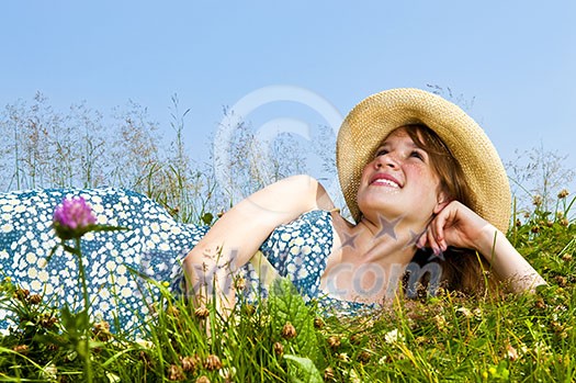 Young teenage girl laying on summer meadow in straw hat looking up