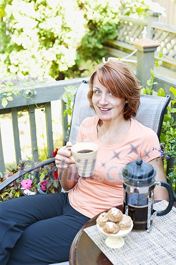 Happy woman relaxing with coffee and cookies on deck chair in backyard at home