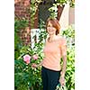 Happy middle aged woman gardening and pruning rose bush with garden shears