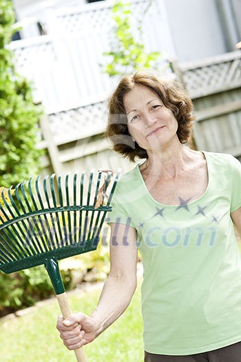 Senior woman smiling holding rake for yard work outside