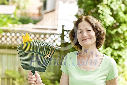 Senior woman smiling holding rake for yard work outside