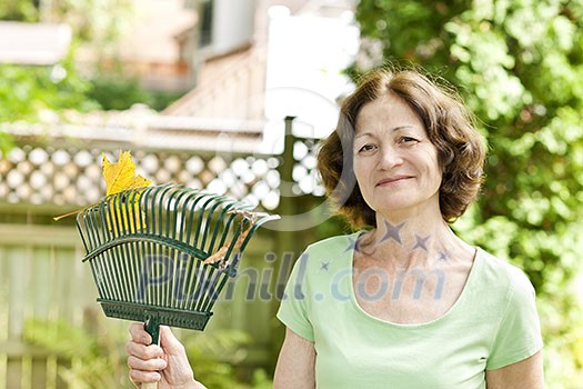 Senior woman smiling holding rake for yard work outside Senior woman smiling holding rake for yard work outside