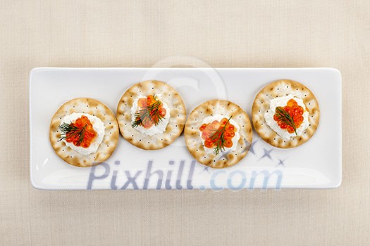 Caviar appetizer with goat cheese and crackers on white plate from above