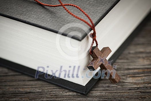 Closeup of wooden Christian cross necklace next to holy Bible Closeup of wooden Christian cross necklace next to holy Bible
