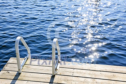Dock and ladder on calm summer lake with sparkling water in Ontario Canada Dock and ladder on calm summer lake with sparkling water in Ontario Canada