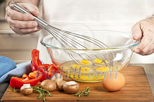 Closeup on man's hands whisking eggs in bowl for cooking omelet with vegetables Closeup on man's hands whisking eggs in bowl for cooking omelet with vegetables