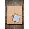 Gift package and card in brown paper wrapper tied with string on rustic wood background