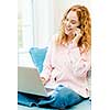 Smiling caucasian woman using laptop computer while on cellphone at home