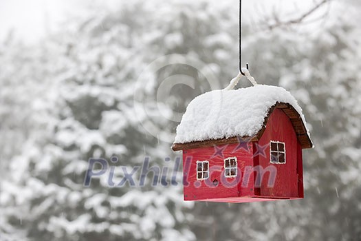 Red bird house hanging outdoors in winter covered with snow