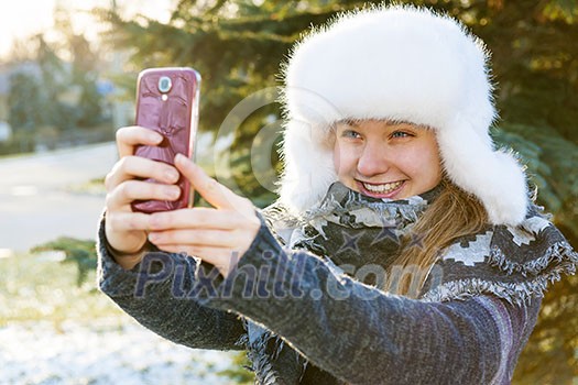 Portrait of teenage girl taking selfie picture with mobile phone outside in winter