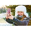 Portrait of teenage girl taking selfie picture with mobile phone outside in winter