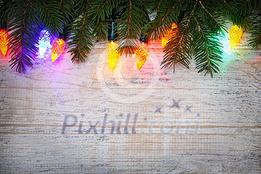 Multicolored Christmas lights on spruce branch with wooden background