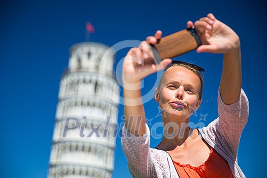 Gorgeous young woman taking a selfie with her smart phone in front of the Leaning Tower of Pisa, Tuscany, Italy (shallow DOF)