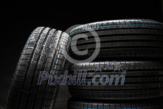 Stack of brand new high performance car tires on clean low-key black studio background