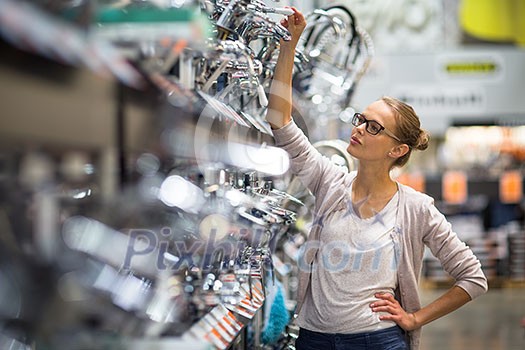 Pretty young woman choosing a bathroom/kitchen tap in a home furnishings retail store Pretty young woman choosing a bathroom/kitchen tap in a home furnishings retail store
