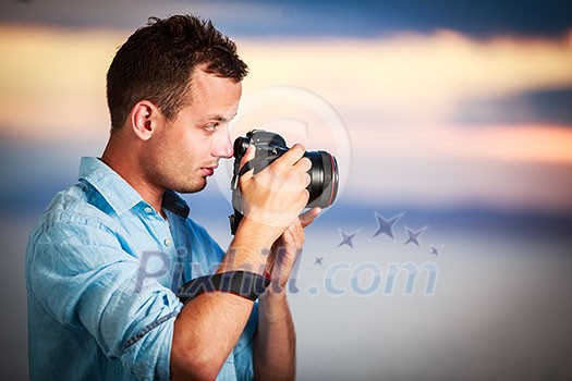 Handsome young photographer using his modern DSLR outdoors, against lovely sky backdrop (color toned image;shallow DOF) Handsome young photographer using his modern DSLR outdoors, against lovely sky backdrop (color toned image;shallow DOF)