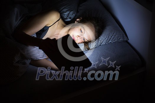 Young woman using tablet computer in bed late at night (color toned image; shallow DOF)