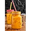 Fresh orange juice with ice in a mason jar on wooden table