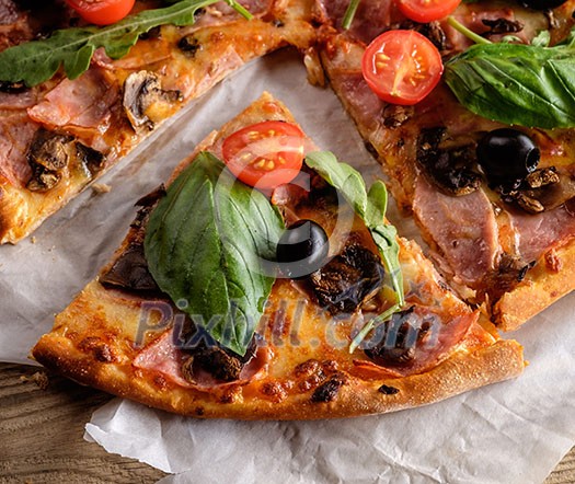 A slice of pizza with bacon, tomatoes, basil and arugula (salad rocket) on a wooden table