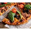 A slice of pizza with bacon, tomatoes, basil and arugula (salad rocket) on a wooden table