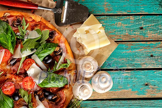 Homemade delicious pizza with bacon, tomatoes, olives and basil top view over wooden background