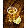 Gold tequila shot with lime on wooden background, selective focus.