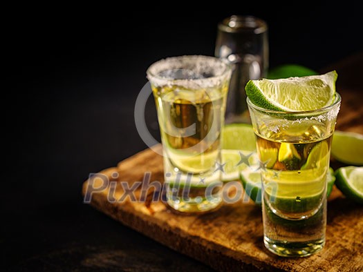 Two Gold tequila shots with lime, copy space on left side. Gold Mexican tequila on wooden background. Alcohol drink, selective focus.
