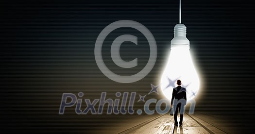 Back view of businessman looking at big glowing light bulb Back view of businessman looking at big glowing light bulb